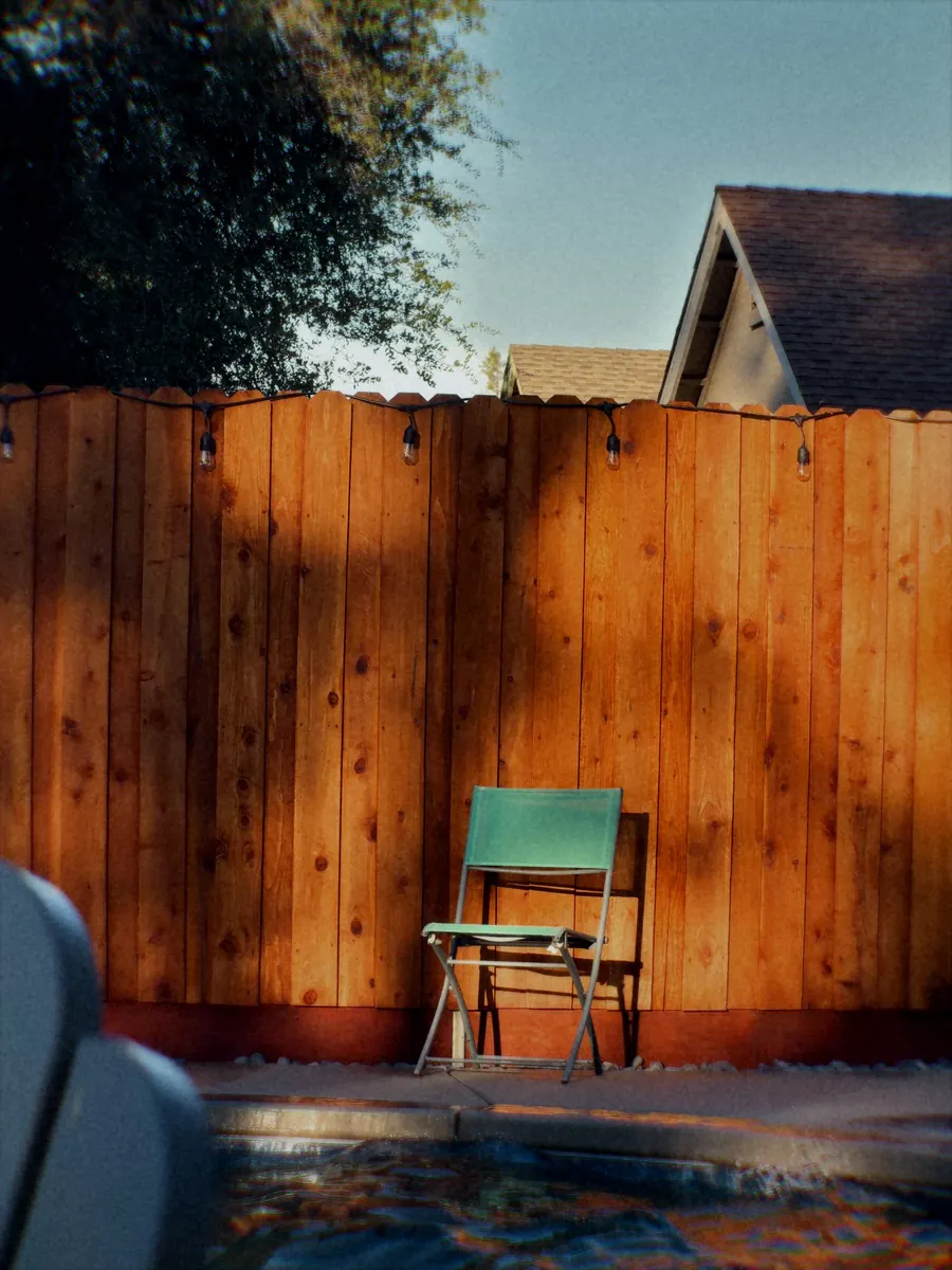 A green folding chair against a redwood fence in a backyard